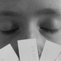 Grayscale close-up photo of a young woman's face. She is holding a number of scented paper strips in front of her nose.