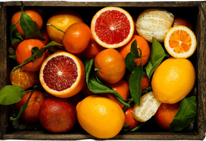 A wooden box filled with leaves and citrus fruit including oranges, lemons, grapefruit, blood oranges, and clementines.