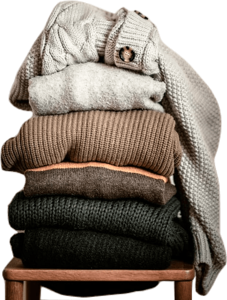 A pile of neutral-toned chunky-knit cashmere sweaters on a wooden stool.