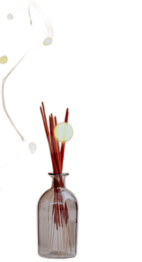 A number of red-tipped incense sticks in a glass jar, with golden bokeh sparkles floating around it.