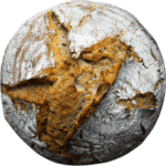 A round brown loaf of homemade sourdough bread, lightly powdered with white flour.