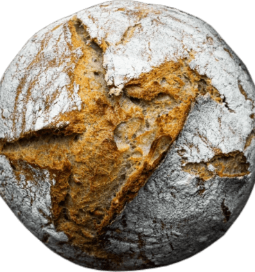 A round brown loaf of homemade sourdough bread, lightly powdered with white flour.