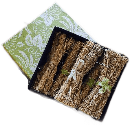 A green and white origami paper box containing many small bundles of dried vetiver grass tied with strips of cloth and twine.