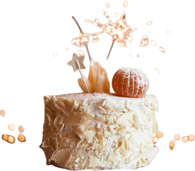 A white cake covered in shavings of white chicolate, with a clementine and several lit sparklers on top of it.