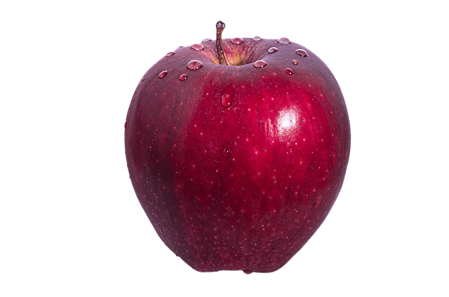 A shiny, bright red delicious apple, with a few drops of water resting on top of it.