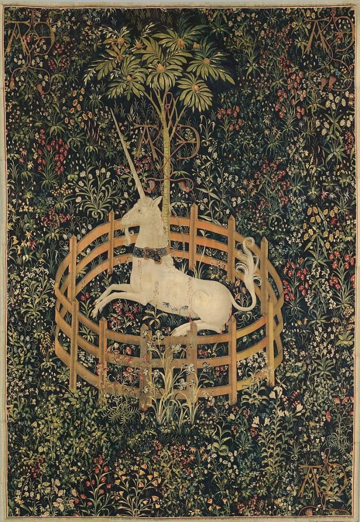 Medieval tapestry of a white unicorn in a circular fence on a backdrop of myriad green plants and muted-colored wildflowers.