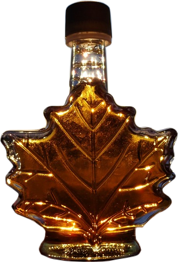 A glass bottle shaped like a maple leaf with a black cap filled with golden amber-colored maple syrup, backlit by sun.