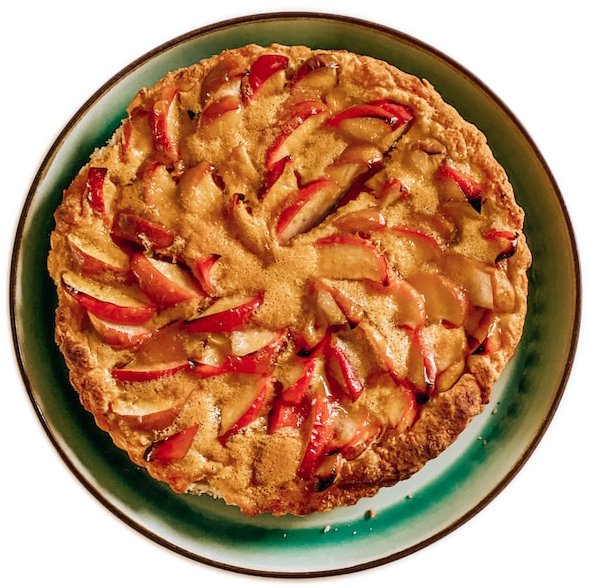 A light-brown apple pie decorated ornately with red apple slices on a green, white, and brown round dish.