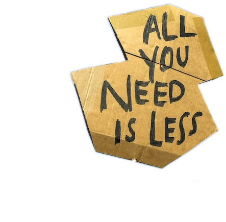A cardboard sign hand-painted with the words "All you need is less" in black letters.