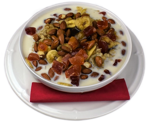 A white bowl filled with oatmeal with milk, topped with almonds and chopped dried fruit.