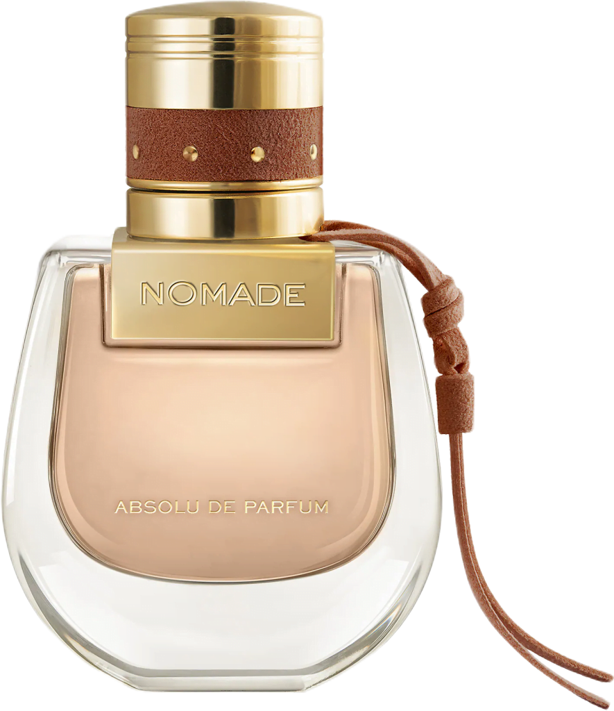 A glass bottle of Nomade Absolu shaped like a saddle bag filled with blush pink liquid with a gold cap and leather strap.